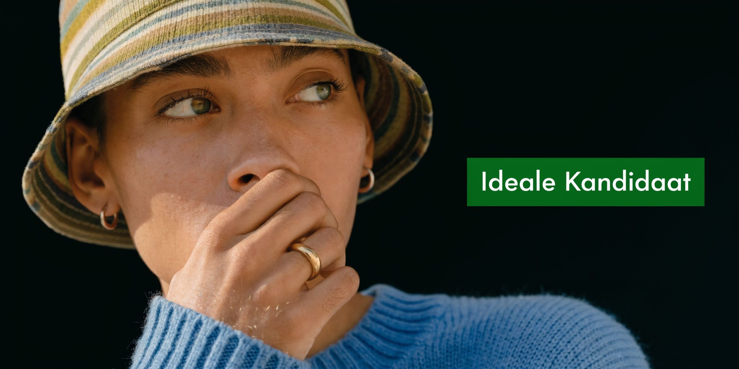 Een persoon met een gestreepte hoed kijkt peinzend weg met een hand voor de mond geplaatst.